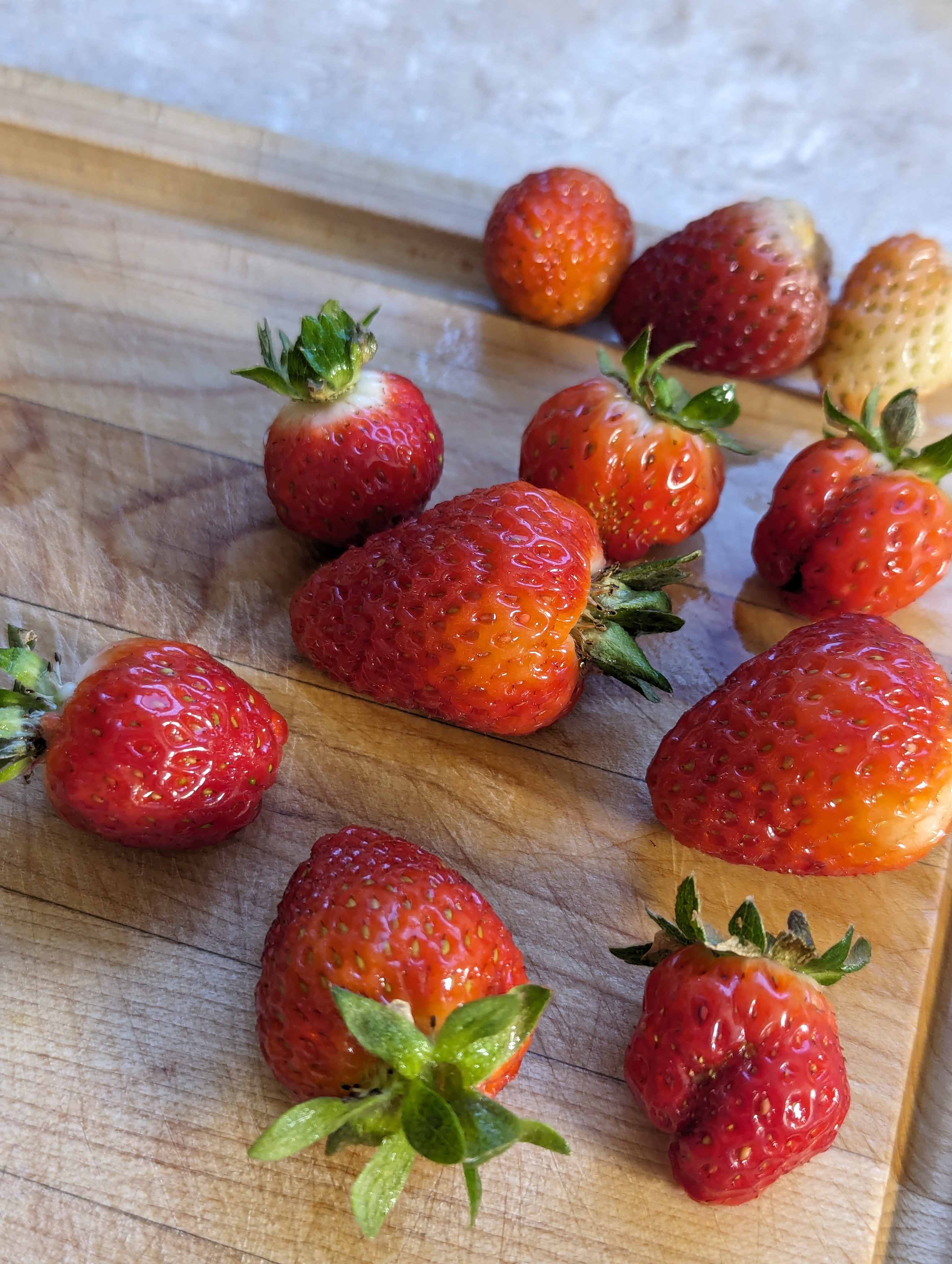 A handful of ripe strawberries on a wooden cutting board.